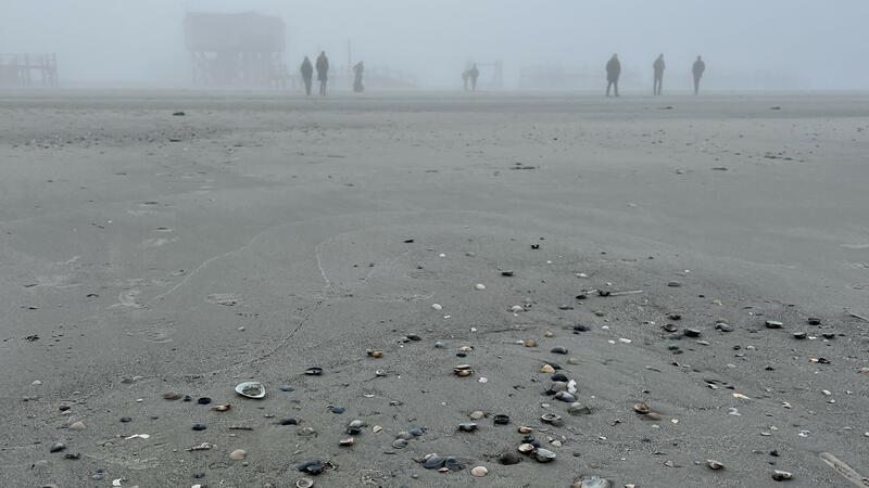 Beach in fog with people and wooden building in the distance. © CWSS/Bostelmann